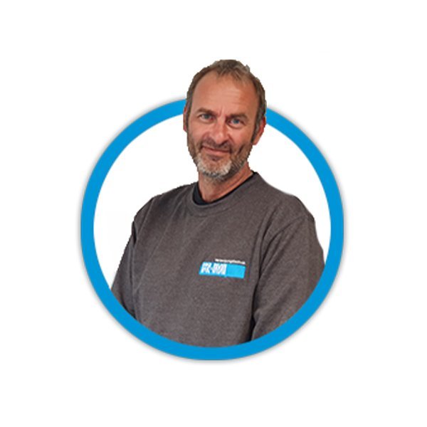 Ein Mann mit Bart und lächelndem Gesicht trägt ein graues Sweatshirt mit einem blauen Logo, vor einem weißen Hintergrund.